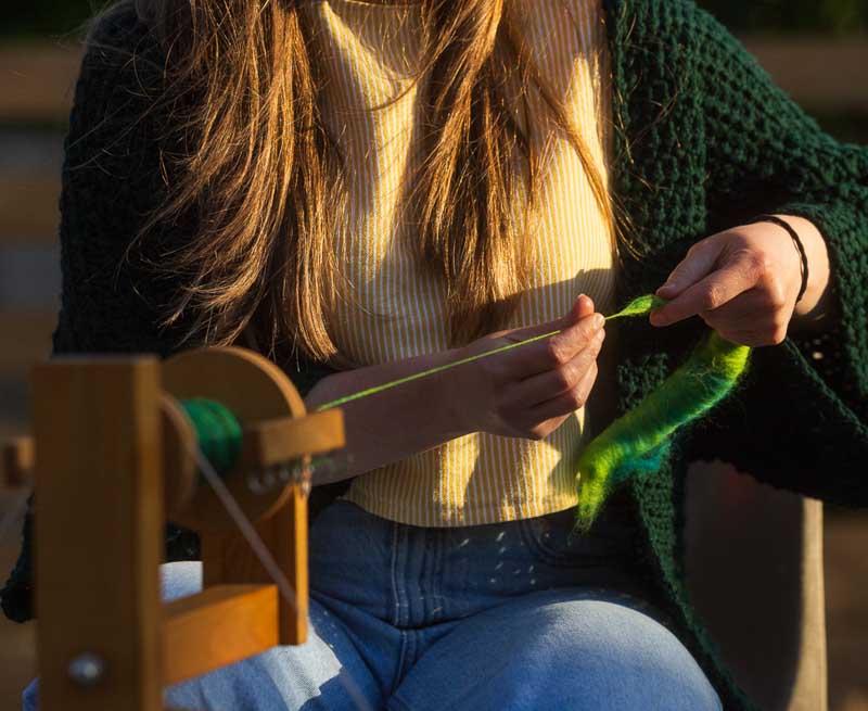 Un personnage filant de manière traditionnelle de la laine verte sur son rouet